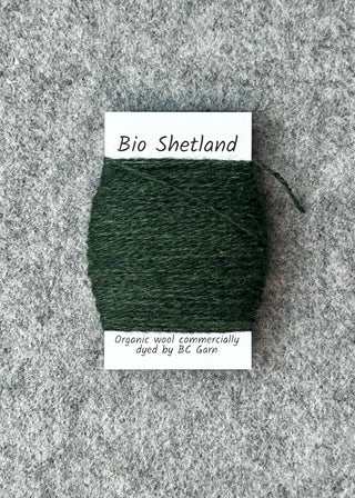 Bobbin of dark green yarn with a label on a textured gray background