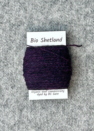 Bobbin of dark purple yarn with a label on a textured gray surface