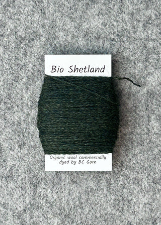 Bobbin of dark green yarn with a label on a textured gray background