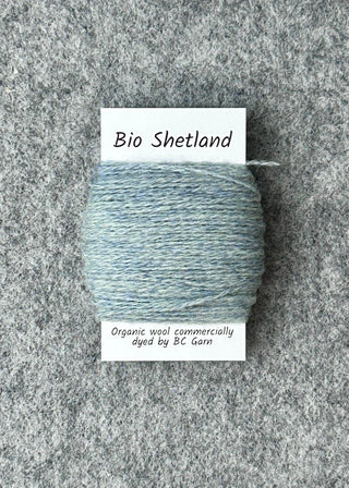Bobbin of light blue yarn labeled 'Bio Shetland' on a textured gray background